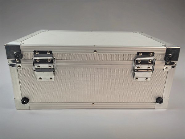 Rear hinge side of aluminum transport case Rear view of a silver aluminum case showing two hinges, riveted frame edges, and corner feet