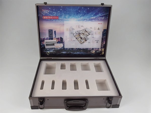 Open aluminum display case for electrical switches, showing custom white foam inserts with multiple cutouts and a printed interior lid panel featuring a building layout and product images.